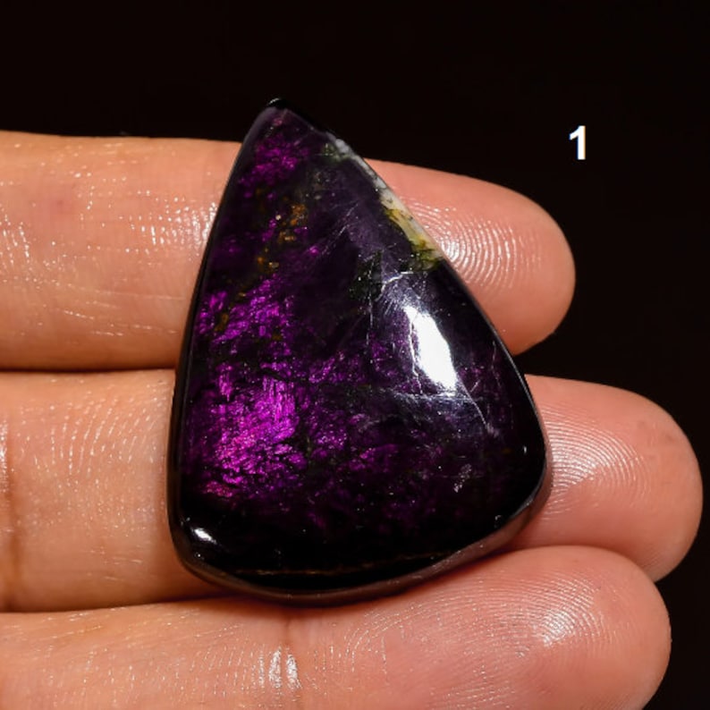 May include: A dark purple and black gemstone cabochon with a pear shape and a high polish. The stone has a shimmering, iridescent quality.