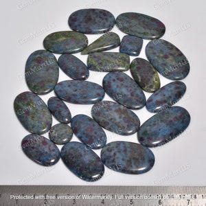 May include: A collection of 20 oval-shaped, polished, blue, green, and red gemstone cabochons. The stones have a speckled pattern and are arranged in a circle on a white surface.