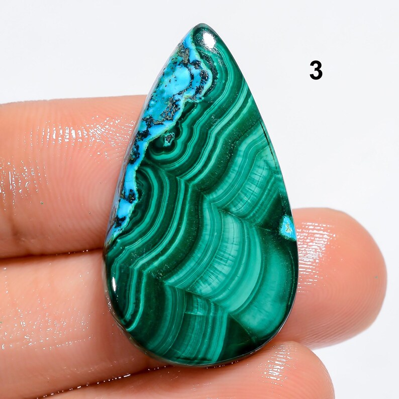 May include: A green and blue gemstone cabochon with a teardrop shape. The stone has a swirling pattern of green and blue.