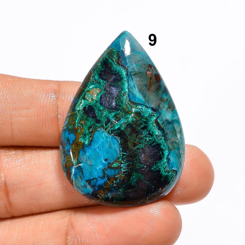 Pu&ograve; includere: Un cabochon di crisocolla a forma di lacrima, di colore blu, verde e marrone. La pietra ha una superficie lucida e liscia e un motivo unico e vorticoso.