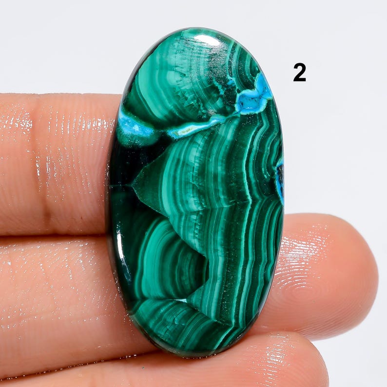 May include: Oval shaped green and blue malachite cabochon gemstone with a swirling pattern.