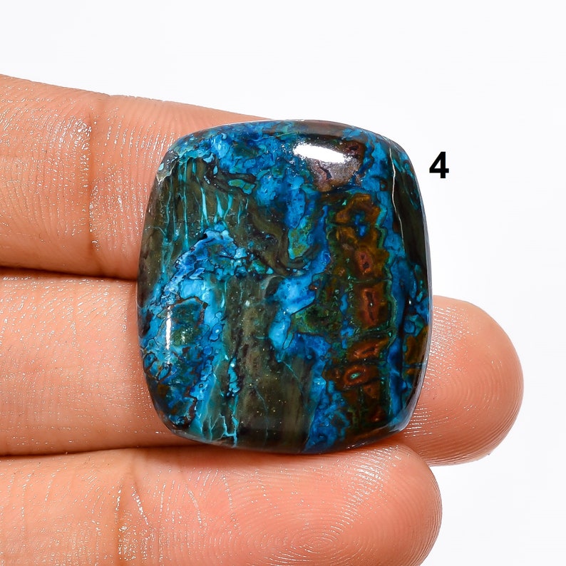 Pu&ograve; includere: Un cabochon di pietra preziosa blu, verde e marrone di forma quadrata. La pietra preziosa presenta un motivo unico di vortici e venature.