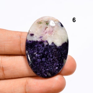 May include: Oval shaped purple and white gemstone cabochon with a rough, textured surface. The stone has a white top with purple and pink swirls and a purple bottom with a rough, textured surface.