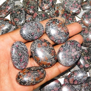 Peut inclure: Une collection de pierres polies de forme ovale avec un motif moucheté noir et blanc et des taches rouges. Les pierres sont lisses et ont une finition brillante.