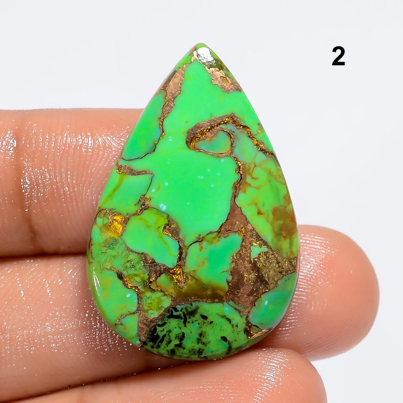 May include: Green turquoise cabochon with copper inclusions in a teardrop shape. The stone has a mottled green and brown pattern.
