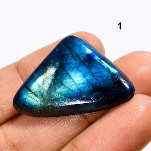 May include: A triangular, blue labradorite gemstone with iridescent flashes of color. The gemstone is smooth and polished, with a dark blue base and lighter blue and green flashes.
