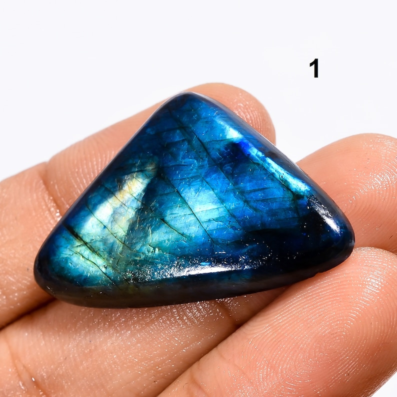 May include: A triangular, blue labradorite gemstone with iridescent flashes of color. The gemstone is smooth and polished, with a dark blue base and lighter blue and green flashes.