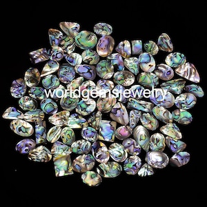 May include: A collection of iridescent abalone shell cabochons in various shapes and sizes. The shells have a beautiful rainbow of colours, including green, blue, purple, and gold.