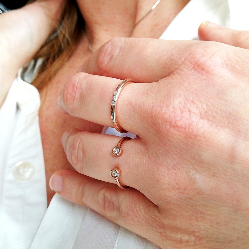 May include: Two rose gold rings with small diamonds. One ring is a simple band with three diamonds, the other is a curved band with two diamonds.