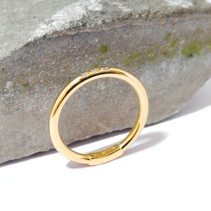 May include: A thin gold band ring with three small diamonds set in the band.