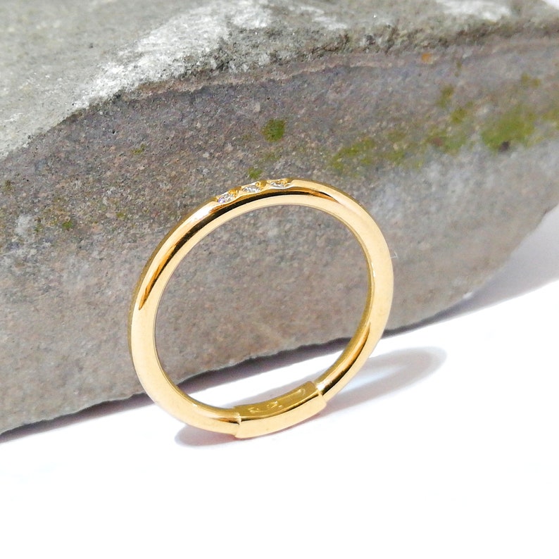 May include: A thin gold band ring with three small diamonds set in the band.