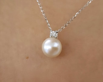 Puede incluir: Un collar con un colgante de perla blanca y un pequeño acento de diamante. El collar está hecho de plata y tiene una cadena delicada.