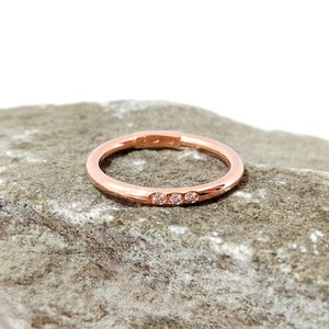 May include: A thin rose gold band with a row of three small diamonds.