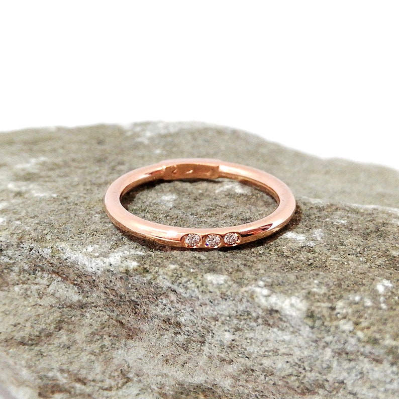 May include: A thin rose gold band with a row of three small diamonds.
