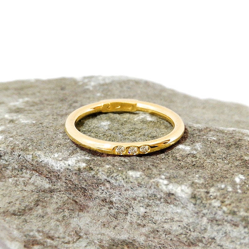 May include: A simple gold band ring with three small diamonds set in a row.