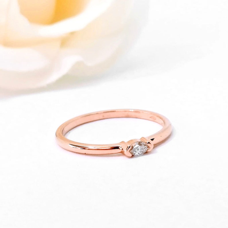May include: A delicate rose gold band ring with a single marquise-shaped diamond.