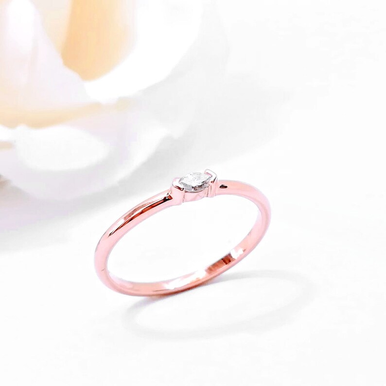 May include: A delicate rose gold band ring with a single marquise-shaped diamond set in the center.