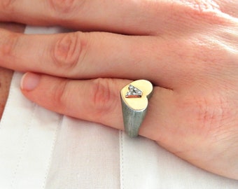 May include: A silver heart-shaped ring with a gold heart inset and a single diamond in the center.