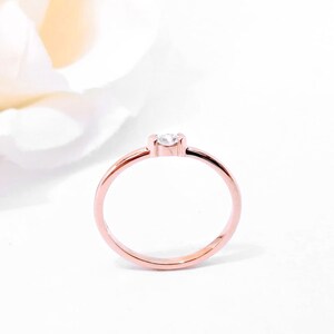 May include: A simple rose gold band ring with a single, small, clear gemstone.