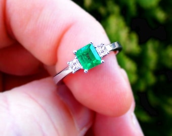 May include: A silver ring with a large emerald green square-shaped gemstone and two smaller diamond-shaped gemstones on either side.