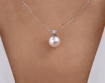 Puede incluir: Un collar de cadena de plata con un solo colgante de perla blanca grande. La perla está acentuada con un pequeño grupo de diamantes claros y brillantes.