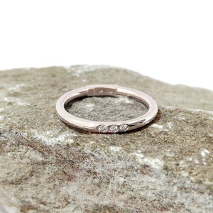 May include: A thin, silver band with three small diamonds set in a row.
