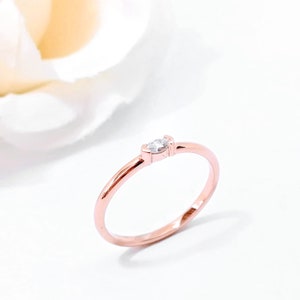 May include: A delicate rose gold ring with a single, small, marquise-shaped diamond.