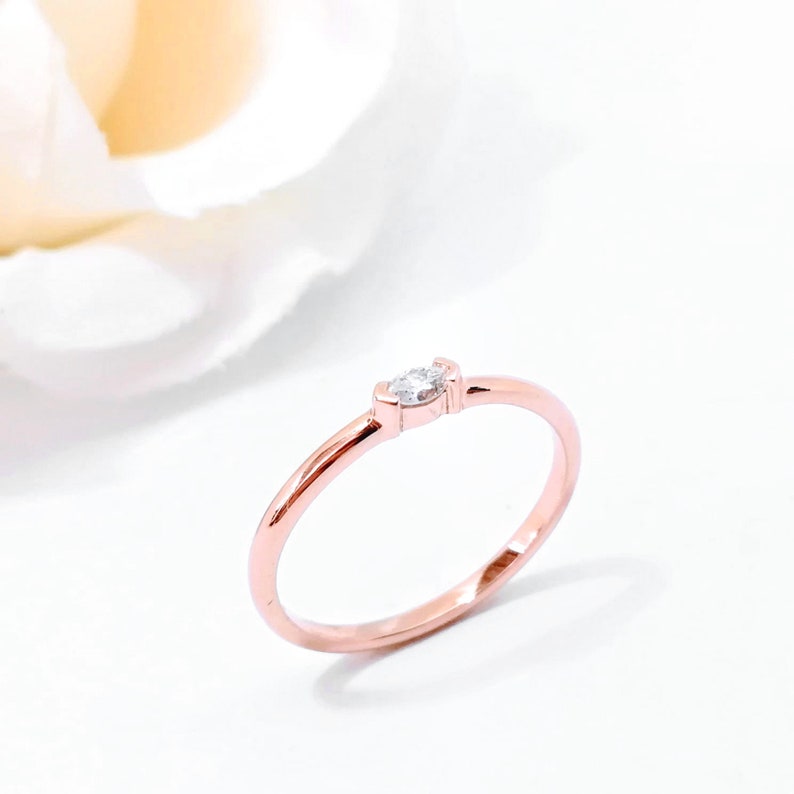 May include: A delicate rose gold ring with a single, small, marquise-shaped diamond.