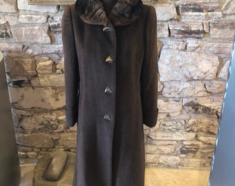May include: A dark brown, full-length coat with a fur collar and matching fur hat. The coat has three decorative buttons and is displayed on a mannequin. The background features a stone wall and a framed painting.
