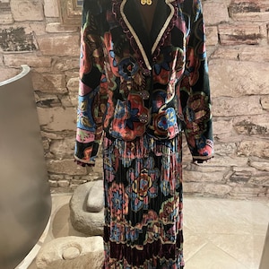 May include: A black velvet jacket and skirt set with a colorful floral pattern. The jacket has a black collar and gold trim. The skirt is pleated and has a ruffled hem.