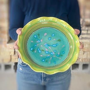 May include: A green ceramic pie plate with a scalloped edge and a blue and pink floral design.