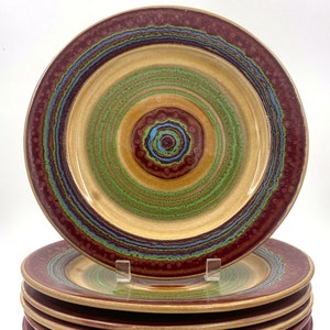 May include: Set of six ceramic dinner plates with a concentric circle design in shades of brown, green, blue, and red.