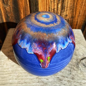 May include: A blue ceramic sphere with a swirling pattern of gold, red, and white. The sphere has a glossy finish and a unique, abstract design.