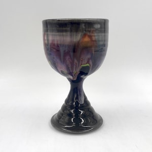 May include: A ceramic goblet with a black base and a purple, pink, and green glaze.