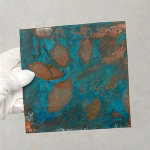May include: A square copper sheet with a blue-green patina and a pattern of brown leaves.