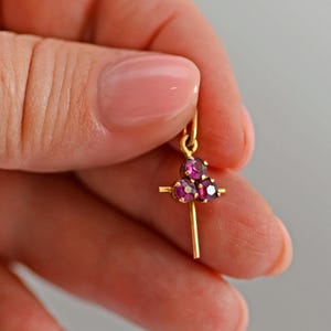 Peut inclure: Un pendentif en or orné de trois pierres rondes à facettes d'un rouge rosé profond, disposées en grappe triangulaire au sommet, avec une fine tige verticale en or descendant du centre et un petit anneau de suspension en or à l'extrémité.