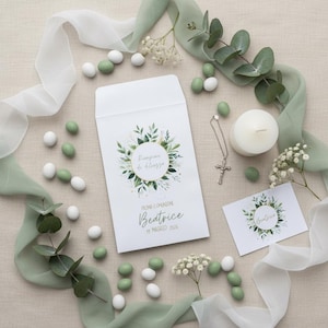 Può includere: Una busta e un biglietto bianchi con un design floreale verde e oro, una collana con una croce d'argento, una candela bianca e confetti verdi e bianchi. La busta recita "Prima Comunione Beatrice 19 Maggio 2026".