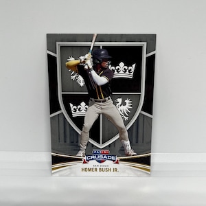 May include: A baseball card featuring Homer Bush Jr. in a batting stance. The card has a gray and white shield design with a crown and eagle. The Panini Crusade logo is visible, along with the text "San Diego".