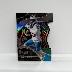 May include: A football trading card featuring Adam Thielen, a wide receiver for the Carolina Panthers. The card has a black background with a holographic design and the text "SELECT 2023 PANTHERS ADAM THIELEN".