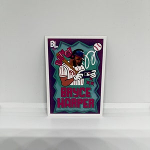 Puede incluir: Una tarjeta de béisbol con una ilustración de dibujos animados de Bryce Harper, un jugador de béisbol de los Phillies de Filadelfia, en un esquema de color morado, azul y rosa. La tarjeta tiene el texto "Bang!" y "Bryce Harper".