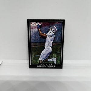 May include: A black framed trading card featuring a football player in a white jersey catching a football. The card has a blue, green, and red background with the text "ARTISTRY ROMEO DOUBS" at the bottom.
