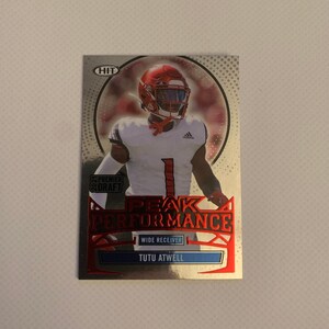 Może przedstawiać: Srebrna i czerwona karta kolekcjonerska futbolu amerykańskiego przedstawiająca piłkarza w czerwonym kasku i koszulce z numerem 1. Na karcie widnieje tekst "2021 PREMIER DRAFT PEAK PERFORMANCE WIDE RECEIVER TUTU ATWELL".