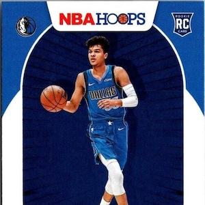 May include: A basketball trading card featuring a blue and white Dallas Mavericks jersey with the name "Dallas" and the number "30" on the front. The player is dribbling a basketball and wearing white socks and black and white sneakers. The card has a blue background with a white border and the text "NBA Hoops" and "Rookie RC Card" in the top corners.