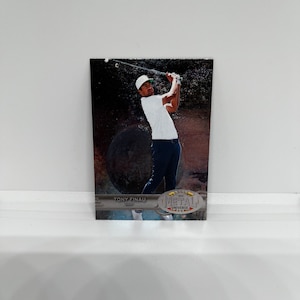 Puede incluir: Una tarjeta de intercambio Panini Metal Universe 2021 con Tony Finau, un golfista profesional. La tarjeta tiene un fondo plateado con un acabado metálico y presenta una foto de Finau balanceando un palo de golf. La tarjeta también incluye el texto "Tony Finau" y "2021 Metal Universe".