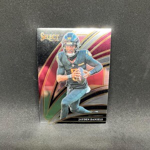 May include: A football trading card featuring Jayden Daniels of the Commanders in a gold Select design. The card shows Daniels in a uniform, holding a football. The card has a glossy finish with a red and gold background.