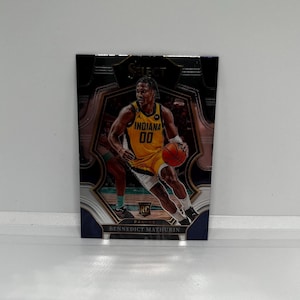 May include: A basketball trading card featuring a player in a yellow and blue jersey with the text "Indiana 00" on the front. The card has a silver, black, and gold design with the text "Select" and "RC" on the front. The player's name, "Benedict Mathurin", is printed on the bottom of the card.