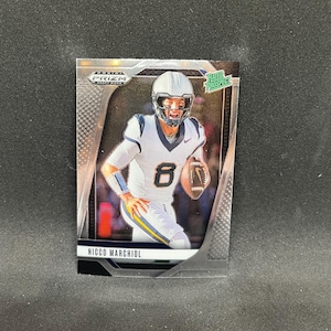 Puede incluir: Una tarjeta de fútbol de Nicco Marchiol de la serie Panini Prizm Draft Picks. La tarjeta presenta a un jugador con uniforme blanco y azul con el número 8, sosteniendo un balón de fútbol. La tarjeta tiene un borde plateado y las palabras "Rated Prospect".