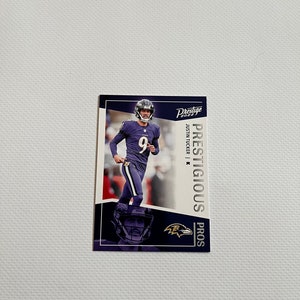 Puede incluir: Una tarjeta coleccionable rectangular con un jugador de fútbol americano con uniforme morado con el número 9. La tarjeta tiene el texto "Prestige" y "Prestigious Pros". El logotipo de los Baltimore Ravens es visible.