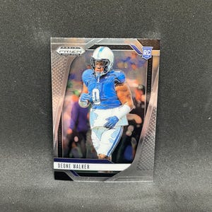 May include: A Deone Walker rookie card from the Prizm Draft Picks series. The card features a player in a blue and white uniform, with the text "DEONE WALKER" at the bottom. The card has a silver border and the RC logo.