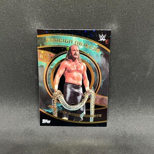 May include: A trading card featuring a wrestler holding a snake. The card has the words "FOREIGN OBJECTS" and "Jake The Snake Roberts" printed on it. The card has a black background with gold and teal accents.